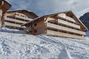 Un hôtel de style chalet en bois, doté de nombreux balcons, situé au pied d’une montagne enneigée.