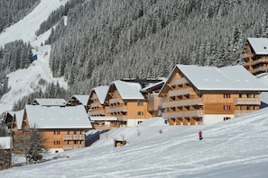 Une rangée de bâtiments de style chalet en bois, dotés de balcons, se dressant sur fond de montagnes enneigées.