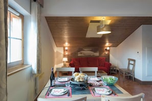 Un coin repas avec une table dressée pour quatre personnes, un canapé rouge en arrière-plan et un plafond en bois.