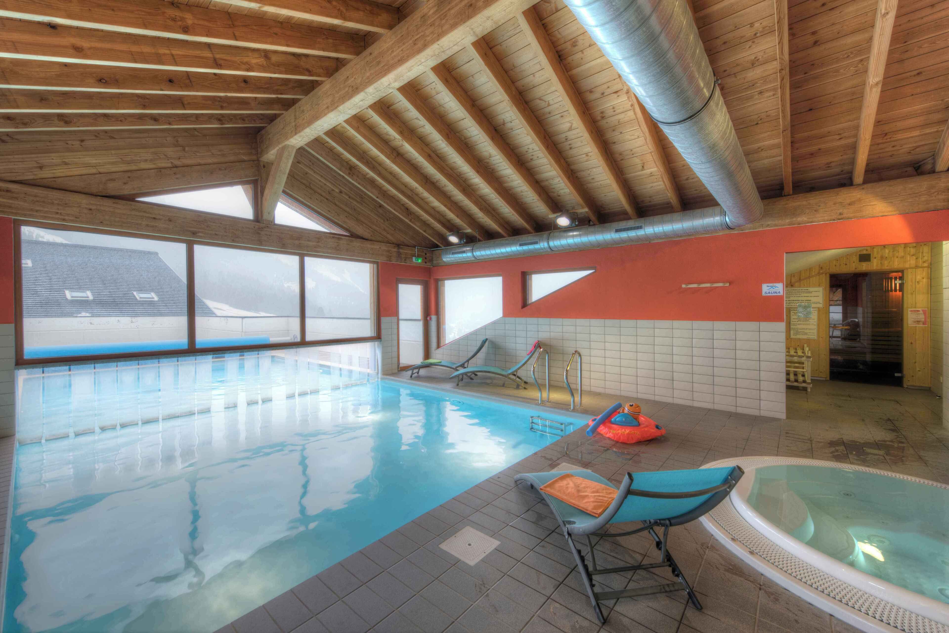 An indoor swimming pool with clear windows, a wooden ceiling, and a small hot tub.