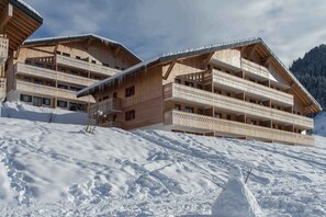 Un hôtel de style chalet en bois, doté de nombreux balcons, situé au pied d’une montagne enneigée.