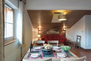 Un coin repas avec une table dressée pour quatre personnes, un canapé rouge en arrière-plan et un plafond en bois.