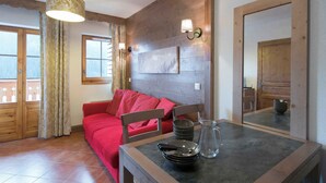 A room with a wooden wall, a red sofa, a dining table with plates and a pitcher, and a window with curtains.