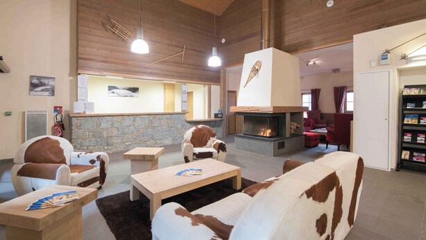 A cozy interior with a stone wall, wooden ceiling, a fireplace, and leather furniture.