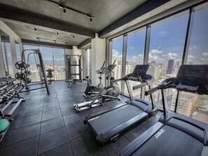 Ein Fitnessstudio mit Laufbändern, Kurzhanteln und Krafttrainingsgeräten, große Fenster mit Blick auf die Stadt.