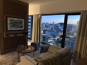 Ein modernes Wohnzimmer mit großem Fenster, einer Couch, einem kleinen Tisch und einem gerahmten Kunstwerk.
