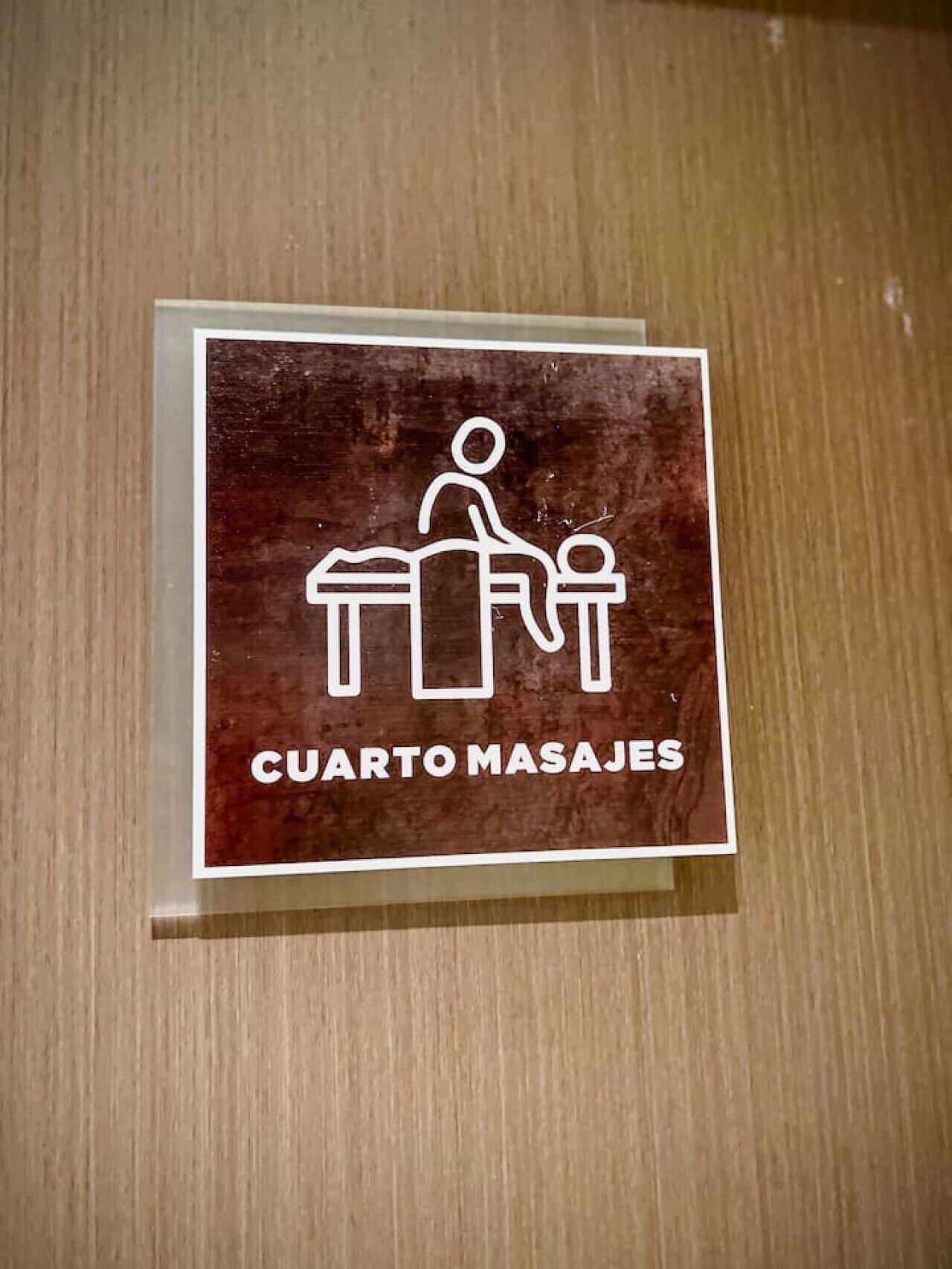 Señal con un icono de masaje y el texto 'CUARTO MASAJES' sobre un fondo de madera.