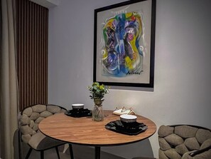 A dining area with a round wooden table, two chairs, a vase with flowers, and a framed abstract painting on the wall. - MStudio 1Bed in heart of Piantini, Santo Domingo (Santo Domingo)