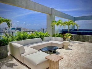 A rooftop terrace with a sectional sofa, a round table, and potted plants. - MStudio 1Bed in heart of Piantini, Santo Domingo (Santo Domingo)