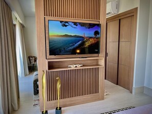 A modern living room with a flat-screen TV mounted on a wooden wall unit, a wooden wardrobe, and a small table with decorative items. - MStudio 1Bed in heart of Piantini, Santo Domingo (Santo Domingo)