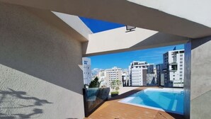 Una terraza en la azotea con piscina, vistas a edificios de la ciudad y cielo despejado.