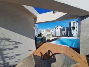 Eine Dachterrasse mit Pool, Blick auf Stadtgebäude und einem klaren Himmel.