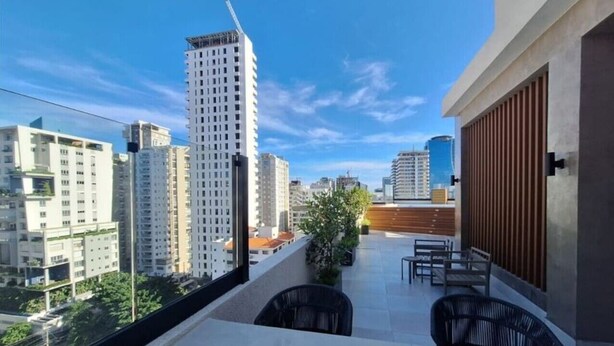Un balcón con vistas a edificios altos, una planta en maceta y mobiliario exterior.