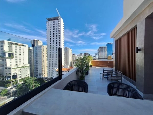 Ein Balkon mit Blick auf hohe Gebäude, einem Topfpflanzen und Gartenmöbeln.