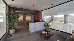 Una recepción moderna con un mostrador de recepción, plantas en macetas y un espacio de descanso.