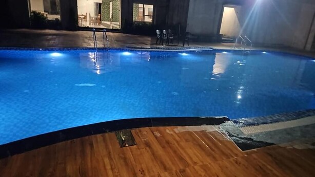 An indoor swimming pool with a wooden deck area, surrounded by walls and a door leading to another room. - Five Elements Corbett Crown Resort (Ramnagar)