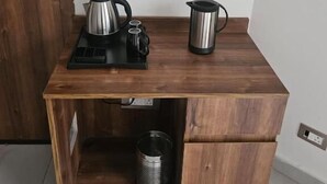 A small wooden desk with a kettle, a coffee pot, and a trash can underneath. - Five Elements Corbett Crown Resort (Ramnagar)