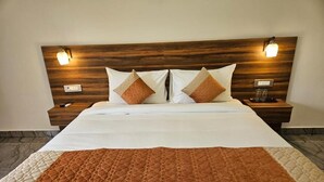 A neatly made bed with a brown quilt, two pillows, and a wooden headboard with wall-mounted lights. - Five Elements Corbett Crown Resort (Ramnagar)
