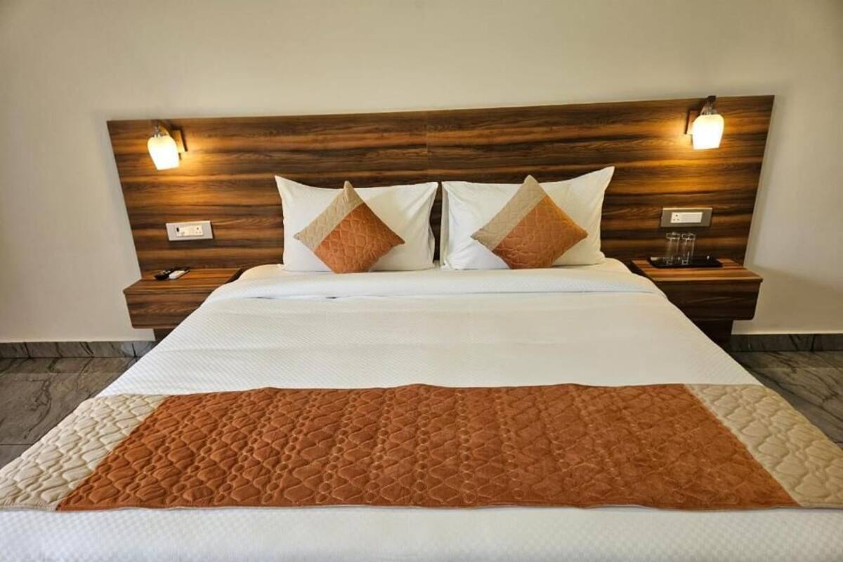 A neatly made bed with a brown quilt, two pillows, and a wooden headboard with wall-mounted lights.