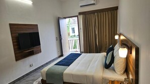 A hotel room with a bed, a TV mounted on the wall, a ceiling fan, an air conditioning unit, and a view of the outside. - Five Elements Corbett Crown Resort (Ramnagar)