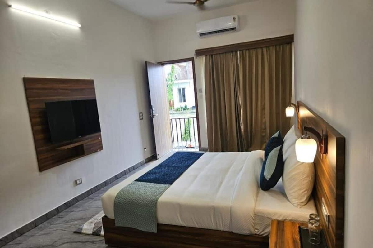A hotel room with a bed, a TV mounted on the wall, a ceiling fan, an air conditioning unit, and a view of the outside.