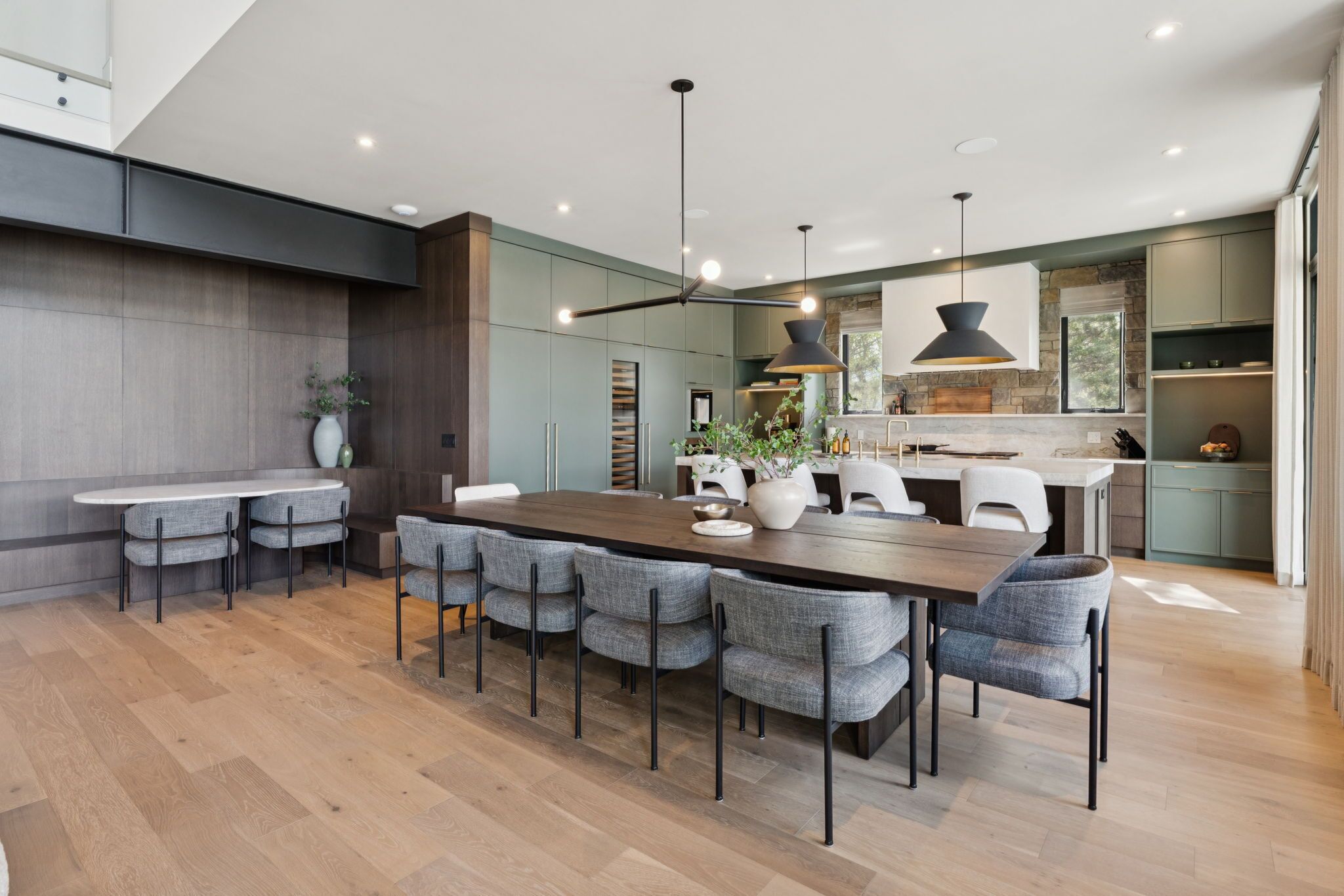 A modern kitchen with a central island, pendant lighting, and a dining area with a long table and chairs.
