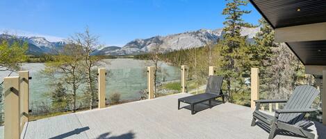 A deck with outdoor seating, overlooking a lake and mountains.