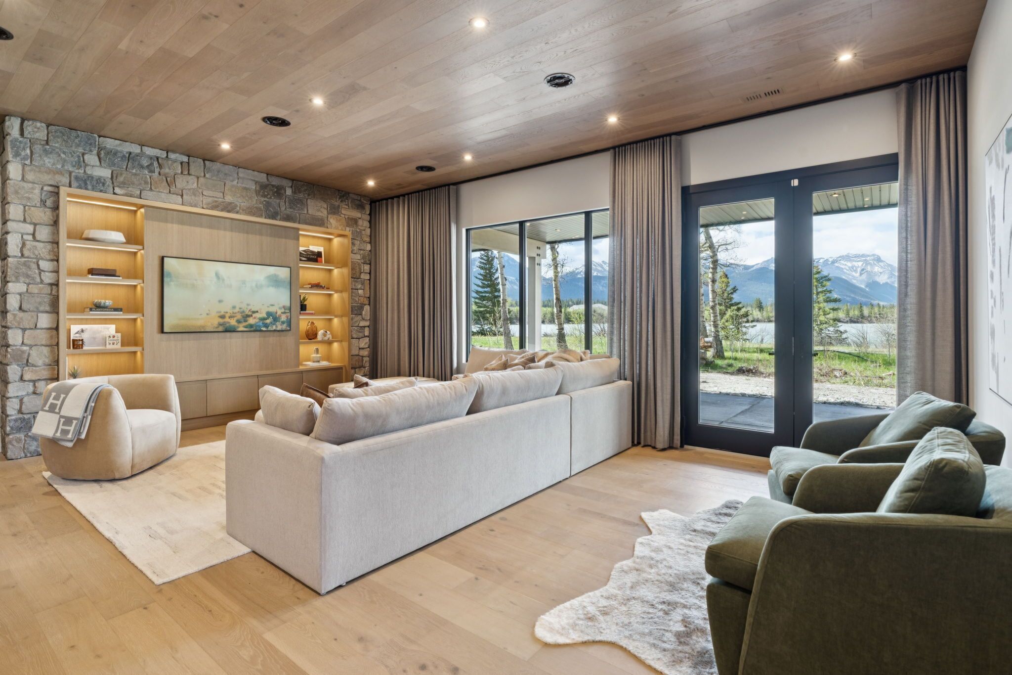 A modern living room with a stone wall, a large sofa, a fireplace, and a view of mountains.