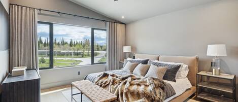 Une chambre moderne avec un grand lit, un banc, une table de chevet et une vue sur un parc.