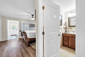A bedroom with a bed, a ceiling fan, and a door leading to a bathroom with a sink and mirror. - Durango 121 pet friendly, private dock (Destin)