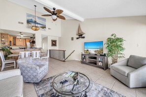 A spacious living room with a sofa, coffee table, and TV. There's a dining area with chairs and a table, and a kitchen in the background. - Durango 121 pet friendly, private dock (Destin)