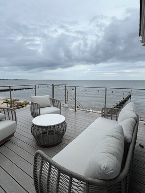 A deck with wicker furniture, a round table, and a view of the sea.