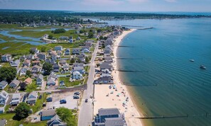 An aerial view of a coastal residential area with houses, a beach, and a pier.