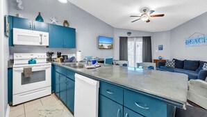 A modern kitchen with blue cabinets, white appliances, and a dining area with a blue sofa. - Private Beach Access, Sleeps 6, Pool & More! (Miramar Beach)