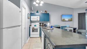 A modern kitchen with a central island, white appliances, blue cabinets, and a seaside view. - Private Beach Access, Sleeps 6, Pool & More! (Miramar Beach)