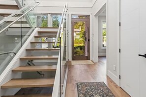 A modern interior with a glass staircase, a wooden floor, and a door leading to an outdoor area with greenery. - Luxury 5-Bed Home, Sleeps 10, Quiet North Delta (Delta)