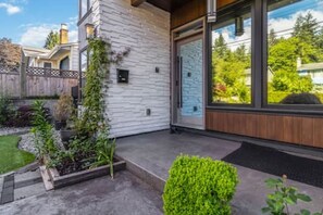 A modern house with a stone exterior, a wooden deck, and a garden with various plants. - Luxury 5-Bed Home, Sleeps 10, Quiet North Delta (Delta)