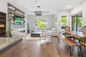 A modern living room with a sofa, a dining table, and a kitchen area with a sink and cabinets. - Luxury 5-Bed Home, Sleeps 10, Quiet North Delta (Delta)