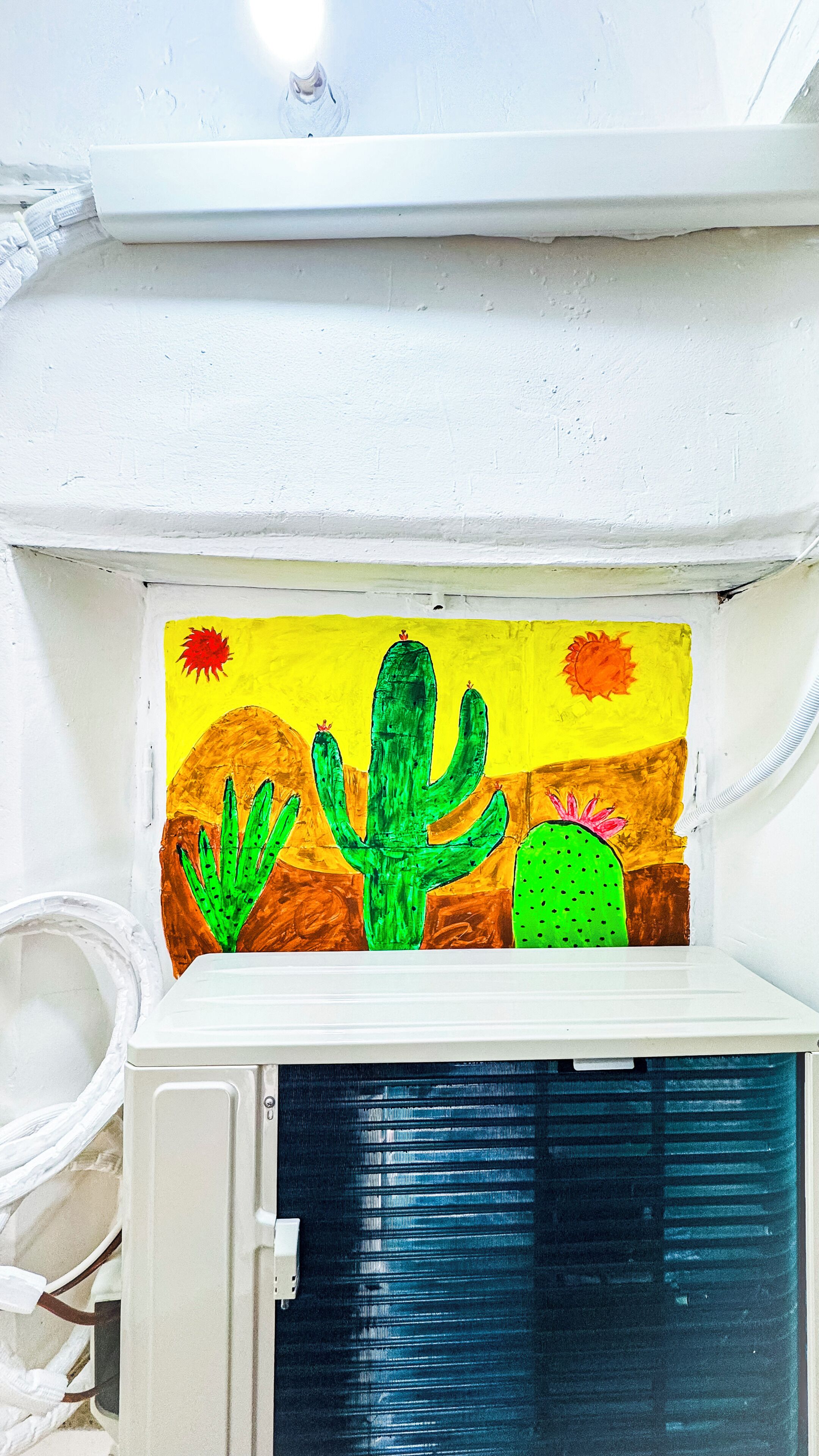 A white wall with a painted mural of a desert scene featuring cacti and a sun.