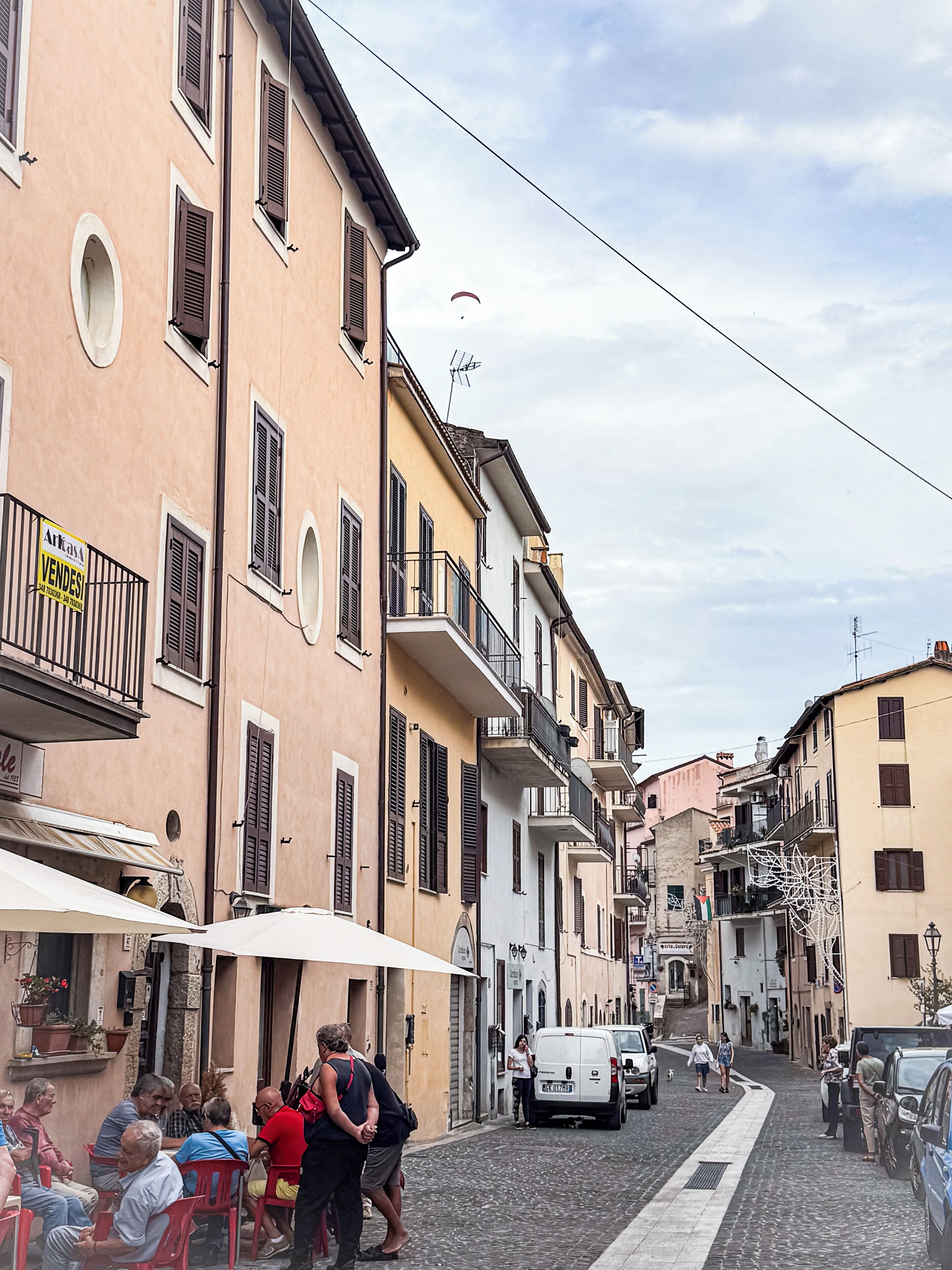 A narrow street lined with traditional buildings, some with balconies and signage indicating local businesses.