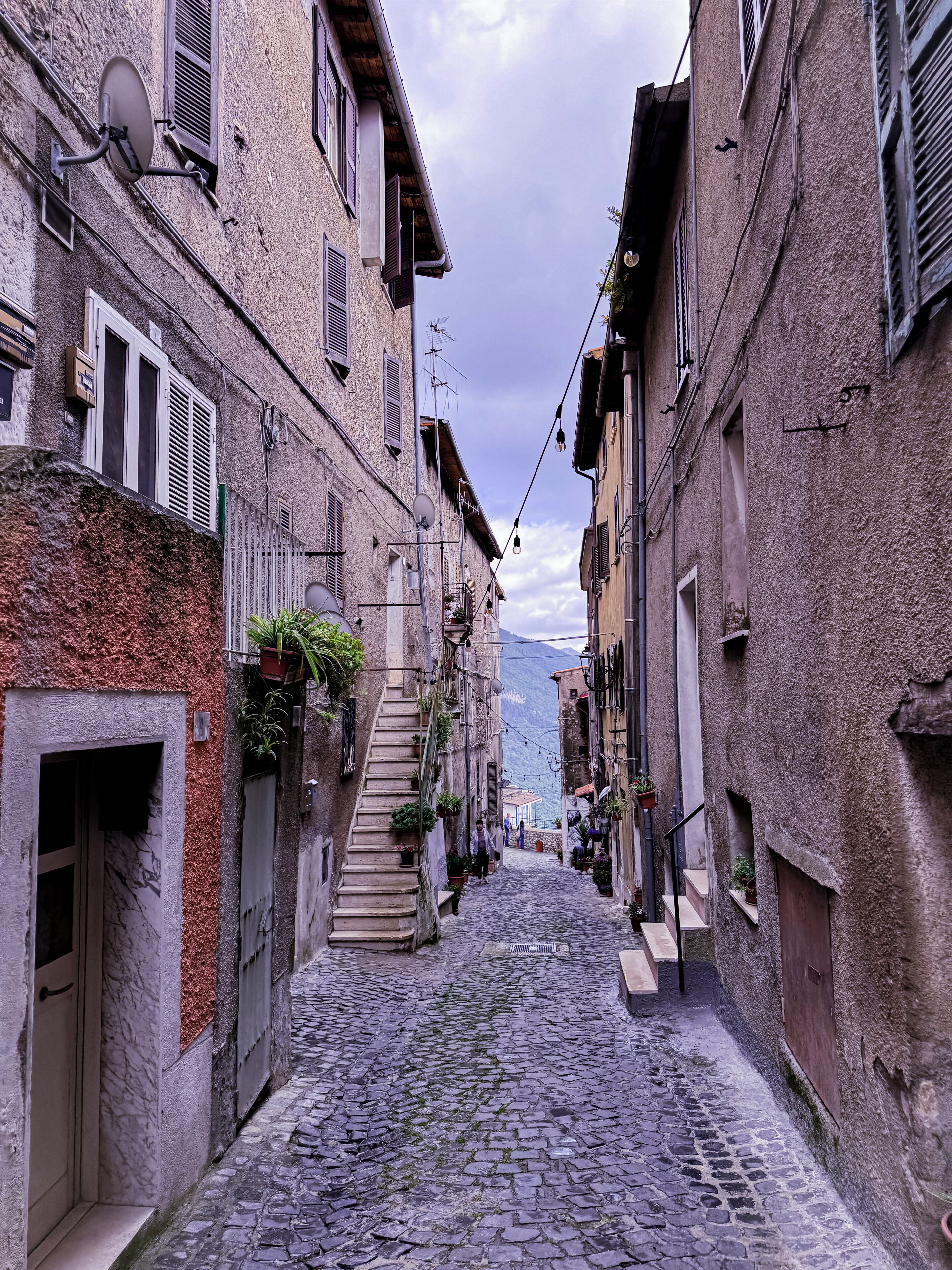 A narrow cobblestone street flanked by historic buildings with balconies and satellite dishes.