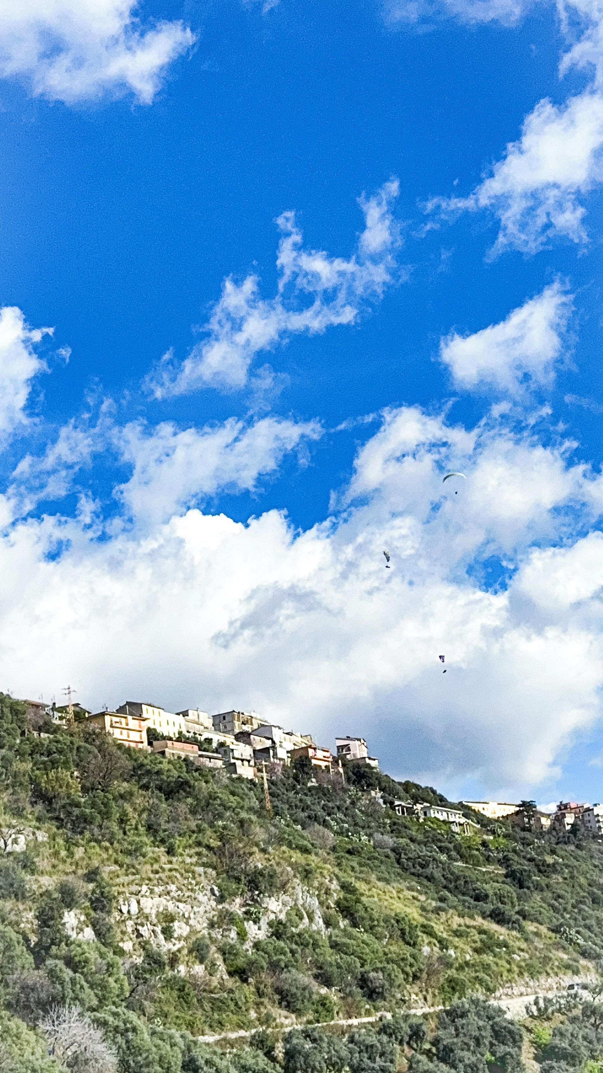 A hillside settlement with buildings, a clear sky, and scattered clouds.