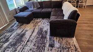 A living room with a sectional sofa, a coffee table, and a patterned rug.