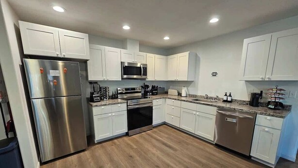 A modern kitchen with white cabinets, stainless steel appliances, and a wooden floor.
