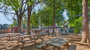A park with picnic tables, playground equipment, and a small building.