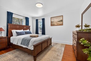 A bedroom with a wooden bed, a nightstand, a dresser, a window with curtains, a painting on the wall, and a plant on the dresser. - Stay on a Farm · Buggy Rides, Goats & Chickens (Bird in Hand)