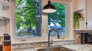 A kitchen with a large window, a sink, and a hanging light fixture.