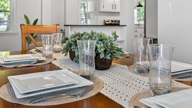 A dining table set with plates, glasses, and a centerpiece of green foliage.