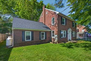 A two-story brick house with a front porch, a garage, and a fenced backyard. - Stay on a Farm · Buggy Rides, Goats & Chickens (Bird in Hand)