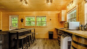 L’intérieur d’un chalet en bois comprend un coin cuisine, un bar avec des tabourets et une grande fenêtre.